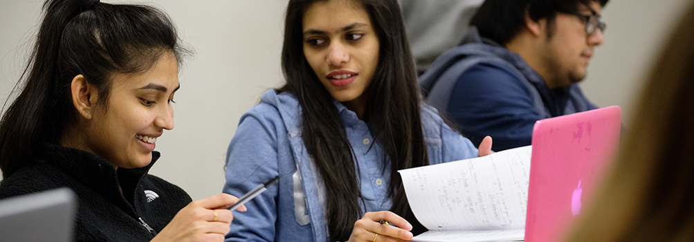 psychology degree seeking students in class reviewing notes together from a notebook
