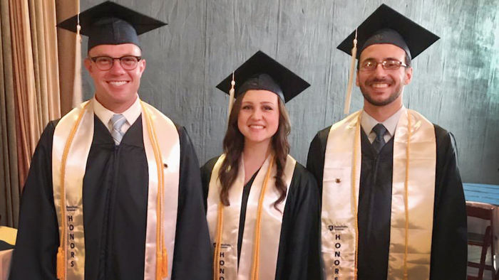  three students pictured wearing cap and gown and white honors sashes and yellow honors cords