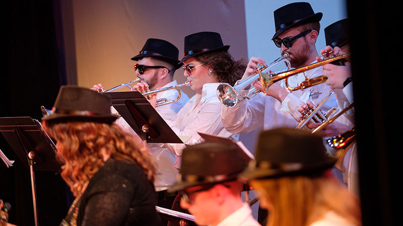Group of students playing brass instruments, wearing hats and sunglasses.
