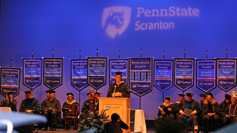 man at a podium with penn state scranton stage party behind him