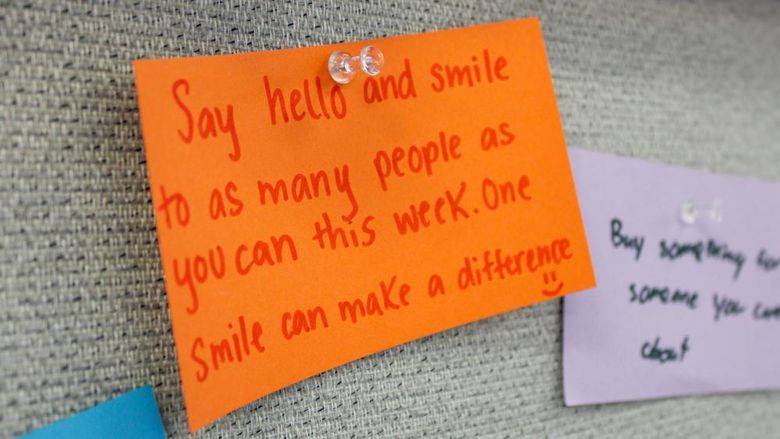 A post it note with a message to be kind is displayed on a bulletin board
