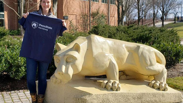 Kailee Shotto stands next to the Harrisburg Lion Shrine and holds up a Penn State Harrisburg tee shirt.