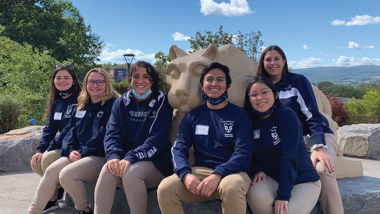6 students in penn state gear gather around the lion shrine statue